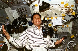 STS-84 Mission Specialist Ed Lu juggles 70mm and 35mm cameras on shuttle's flight deck. 